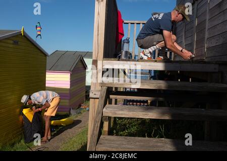 Da ein Nachbar Strandausrüstung einpackt, sorgt ein anderer dafür, dass alle Türen und Schlösser auf einer Strandhütte an der Strandpromenade am 18. Juli 2020 in Whitstable, Kent, England, gesichert sind. Stockfoto