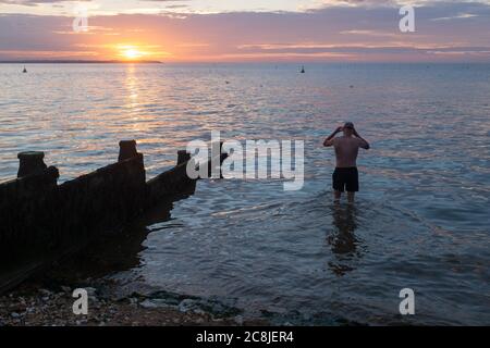 Während die Sonne über dem verblassenden Tageslicht und dem ruhigen Wasser der Themse-Mündung untergeht, taucht ein wilder Schwimmer am 18. Juli 2020 in Whitstable, Kent, England, für sein regelmäßiges Abendbad ins Wasser. Stockfoto