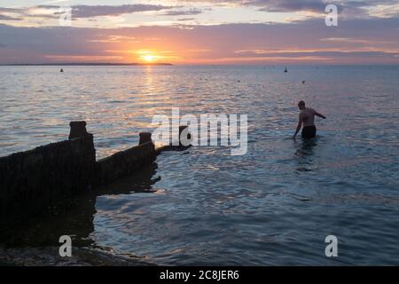 Während die Sonne über dem verblassenden Tageslicht und dem ruhigen Wasser der Themse-Mündung untergeht, taucht ein wilder Schwimmer am 18. Juli 2020 in Whitstable, Kent, England, für sein regelmäßiges Abendbad ins Wasser. Stockfoto