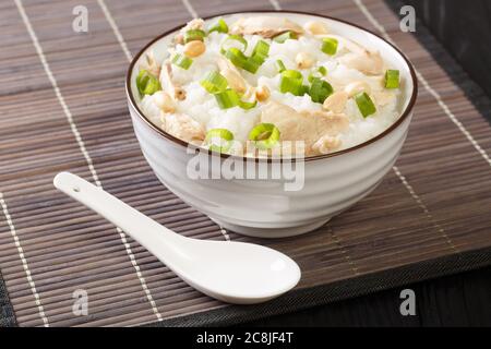 Langsam gekochter Ingwer-Reisbrei mit Huhn, Erdnüssen und grünen Zwiebeln in einer Schüssel auf dem Tisch. Horizontal Stockfoto