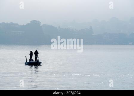 An einem nebligen Wintermorgen stehen zwei Männer in einem Kleines offenes Fischerboot in der Nähe von Cockatoo Island mit Angelruten Im ruhigen Hafenwasser Stockfoto