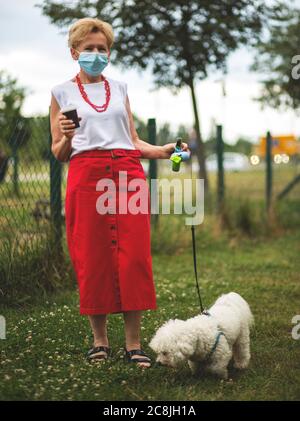 Porträt einer schönen Blondine Frau trägt eine Maske. Menschen zu Fuß Hunde, während Covid-19 Pandemie, im Freien. Stockfoto