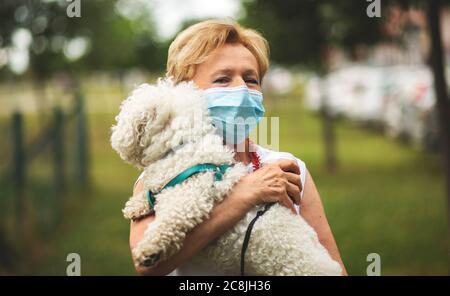 Porträt einer schönen Blondine Frau trägt eine Maske. Menschen zu Fuß Hunde, während Covid-19 Pandemie, im Freien. Stockfoto