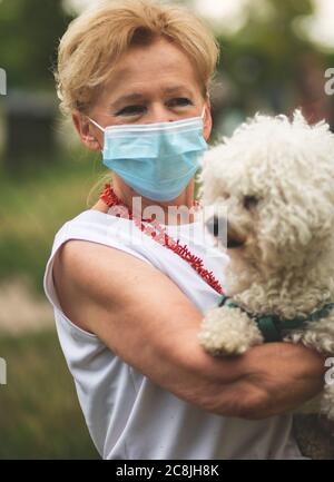 Porträt einer schönen Blondine Frau trägt eine Maske. Menschen zu Fuß Hunde, während Covid-19 Pandemie, im Freien. Stockfoto