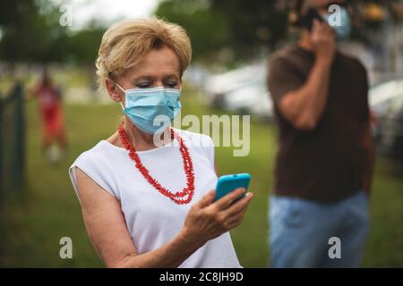 Porträt einer schönen Blondine Frau trägt eine Maske. Menschen zu Fuß Hunde, während Covid-19 Pandemie, im Freien. Stockfoto