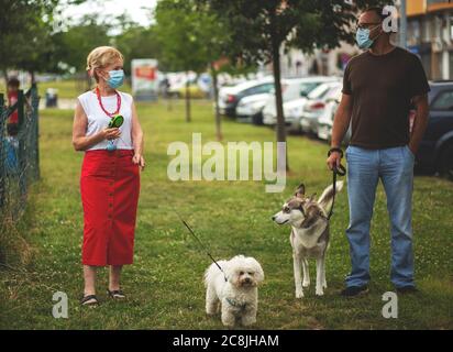 Porträt einer schönen Blondine Frau trägt eine Maske. Menschen zu Fuß Hunde, während Covid-19 Pandemie, im Freien. Stockfoto