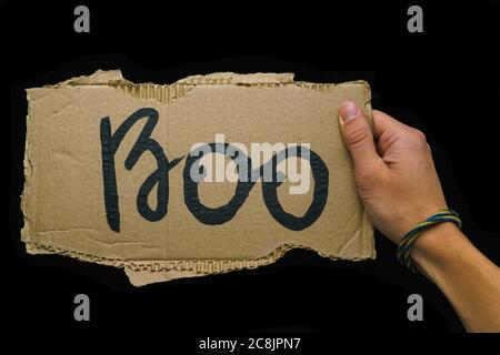 Der Kerl hält in seiner Hand ein Pappschild mit der Aufschrift Boo in schwarzer Farbe auf dunklem Hintergrund gezeichnet, das Konzept des Feiertags Halloween Stockfoto