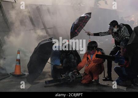 Portland, USA. Juli 2020. Aktivisten decken sich hinter Regenschirmen, als ein Protestler mit einem Laubbbläser Tränengas am 24. Juli 2020 am Eingang zum Bundesgericht in Portland, Oregon, in Richtung Bundesbeamte zurückleitet. Der Bundesschutzdienst erklärte eine rechtswidrige Versammlung und startete eine Flut von Tränengas und Massenkontrollmunition, um Demonstranten vom Zaun zurückzudrängen, der den Zugang zum Eingang des Gebäudes blockierte. (Foto: Alex Milan Tracy/Sipa USA) Quelle: SIPA USA/Alamy Live News Stockfoto