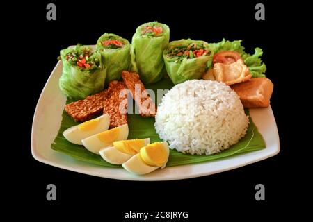 Traditionelles indonesisches Gericht aus Reis, Frühlingsrollen mit Gemüse, gebratenen Tempeh und hart gekochten Eiern, isoliert auf schwarzem Hintergrund. Stockfoto