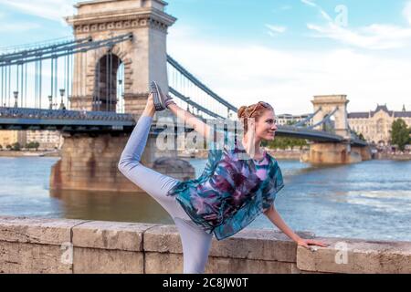 Junge Rotschopf Frau, die Yoga an der Donau in der Stadt, Schwan Pose, Budapest, Ungarn Stockfoto