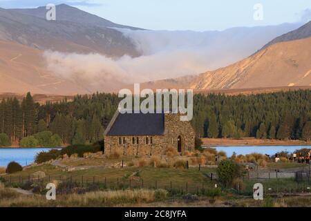 Wolken, die hinter der Kirche des Guten Hirten in Tekapo, Neuseeland, die Berge hinunterströmen. Stockfoto