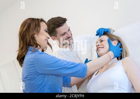 Junge kaukasische männliche Dermatologe mit seiner Krankenschwester Untersuchung ein Gesicht des Patienten Stockfoto