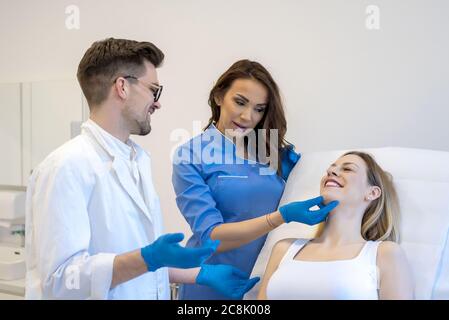 Junger kaukasischer männlicher Dermatologe, der das Gesicht eines weiblichen Patienten mit untersucht Seine Krankenschwester Stockfoto