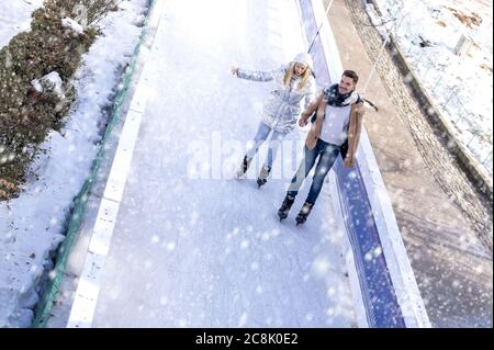 Junge schöne Kaukasion paar Eislaufen und Spaß haben, während Genießen Schneefall im Winter Park Stockfoto
