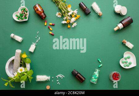 Alternative Pflanzenheilkunde. Homöopathische Globules, frische Wildblumen und Kräuter flach lagen auf grünem Grund. Aromatherapie, Homöopathie Naturprodukt Stockfoto