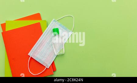 Zurück in die Schule, Coronavirus Tage. Medizinische Schutzmaske, Händedesinfektionsgel und Schulbücher auf pastellgrünem Hintergrund, Draufsicht, Templat Stockfoto