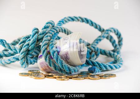 Nahaufnahme eines Bündels von £20 Noten, eingewickelt in altes Seil auf Stapel von losen Wechsel, mit weißem Hintergrund. Konzept, Metapher: Geld für altes Seil. Stockfoto