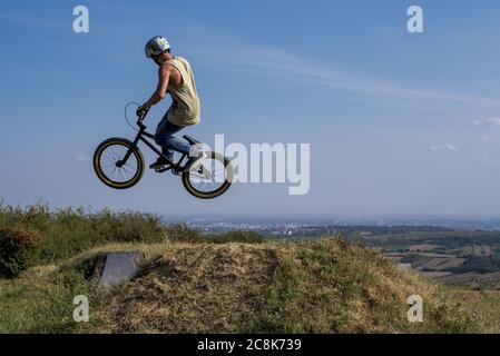 Mann im Helm auf einem Fahrrad springen und fliegen weiter Ein Hügel gegen den blauen Himmel Stockfoto