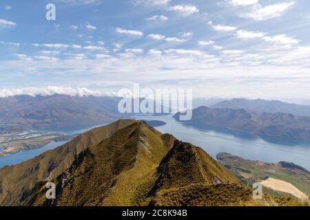 Der Blick vom Roys Peak Lookout über einen Kamm mit Lake Wanaka und weißen Wolken am blauen Himmel. Stockfoto