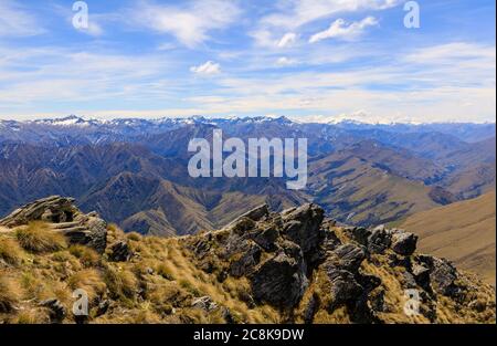 Blick auf die südlichen Alpen vom Aufstieg auf Ben Lomond. Stoßzäpfchen und Felsen im Vordergrund und schneebedeckte Berge im Hintergrund. Stockfoto