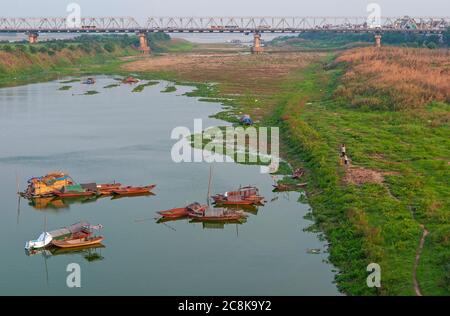 Lange Bien Brücke bei Sonnenuntergang am roten Fluss mit Fischerbooten, Hanoi, Nordvietnam. Stockfoto