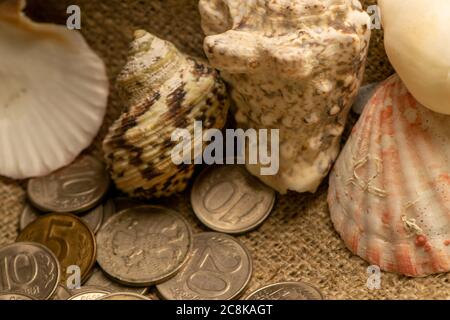 Einige alte Münzen und Muscheln auf dem Hintergrund Stoff mit einer rauen Textur. Nahaufnahme Stockfoto