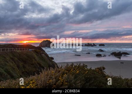 Ende des Tages am Strand ein bisschen Farbe in den dunklen Wolken und die prominenten Felsen kennzeichnet charakteristischen Face Rock State Park, Bandon Oregon Stockfoto