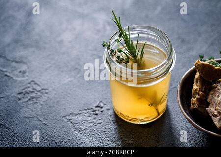 Glasgefäß mit gelber frischer Knochenbrühe auf dunkelgrauem Hintergrund. Gesunde kalorienarme Lebensmittel sind reich an Vitaminen, Kollagen und entzündungshemmende Amino Stockfoto