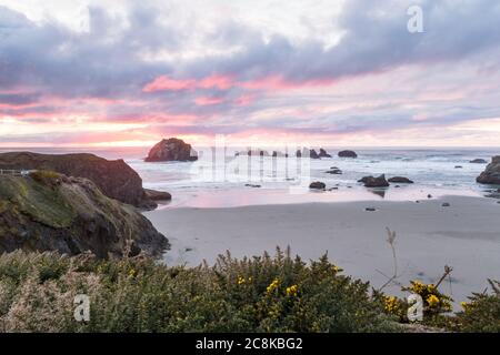 Ende des Tages am Strand ein bisschen Farbe in den dunklen Wolken und die prominenten Felsen kennzeichnet charakteristischen Face Rock State Park, Bandon Oregon Stockfoto