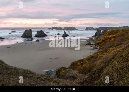 Ende des Tages am Strand ein bisschen Farbe in den dunklen Wolken und die prominenten Felsen kennzeichnet charakteristischen Face Rock State Park, Bandon Oregon Stockfoto