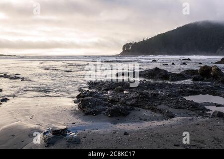 moody Nachmittag an der Küste von Oregon mit niedrigen dichten Wolken mit ein bisschen Licht, das durch die helleren Flecken kommt und sich auf dem Wasser reflektiert Stockfoto