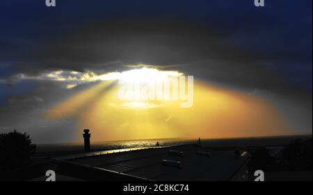 Sonnenstrahlen brechen durch ein Loch in den dunklen Wolken, wenn die Sonne über dem Horizont untergeht. Stockfoto