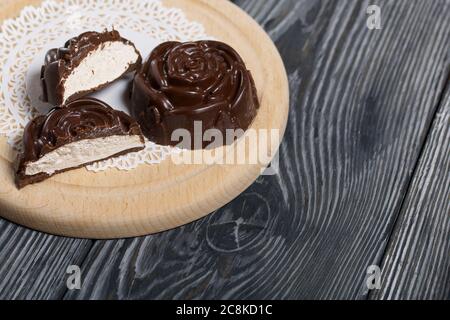 Auf einer weißen Serviette liegt ein in der Form einer Rose gemachtes Schokoladen-Marshmallow. Eine Marshmallow wird halbiert, eine Scheibe ist sichtbar. Stockfoto