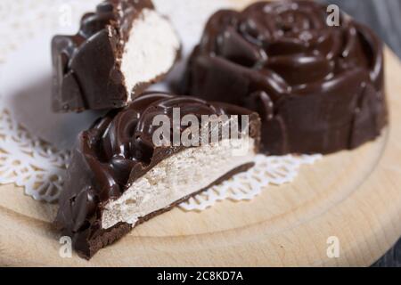 Auf einer weißen Serviette liegt ein in der Form einer Rose gemachtes Schokoladen-Marshmallow. Eine Marshmallow wird halbiert, eine Scheibe ist sichtbar. Nahaufnahme. Stockfoto