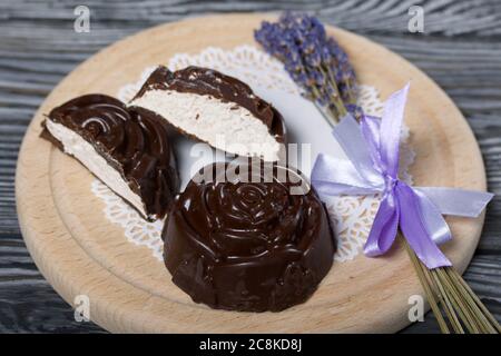 Auf einer weißen Serviette liegt ein zephyr aus Schokolade in der Form einer Rose. Ein zephyr wird halbiert, eine Scheibe ist sichtbar. In der Nähe von einem Bouquet von Lavendel. Stockfoto