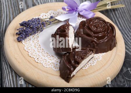 Auf einer weißen Serviette liegt ein zephyr aus Schokolade in der Form einer Rose. Ein zephyr wird halbiert, eine Scheibe ist sichtbar. In der Nähe von einem Bouquet von Lavendel. Stockfoto