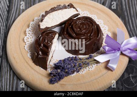 Auf einer weißen Serviette liegt ein zephyr aus Schokolade in der Form einer Rose. Ein zephyr wird halbiert, eine Scheibe ist sichtbar. In der Nähe von einem Bouquet von Lavendel. Stockfoto