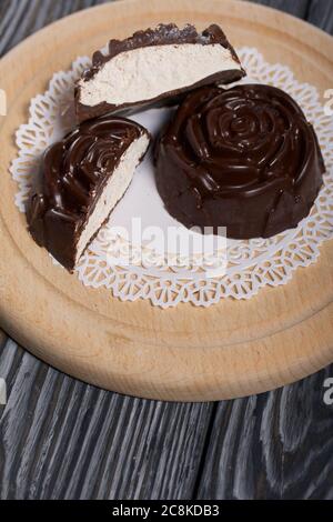 Auf einer weißen Serviette liegt ein in der Form einer Rose gemachtes Schokoladen-Marshmallow. Eine Marshmallow wird halbiert, eine Scheibe ist sichtbar. Stockfoto