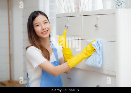 Junge asiatische Frau in Handschuhen Reinigung Haus im Zimmer, Haushälterin ist mit Stoff wischen, Hausmädchen und Service, Arbeiter polieren Staub im Wohnzimmer im Haus, Stockfoto