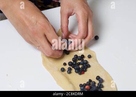 Eine Frau bereitet Knödel mit Heidelbeeren zu. Legt Beeren in gerollten Teig. Nahaufnahme. Stockfoto