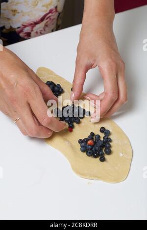 Eine Frau bereitet Knödel mit Heidelbeeren zu. Legt Beeren in gerollten Teig. Nahaufnahme. Stockfoto