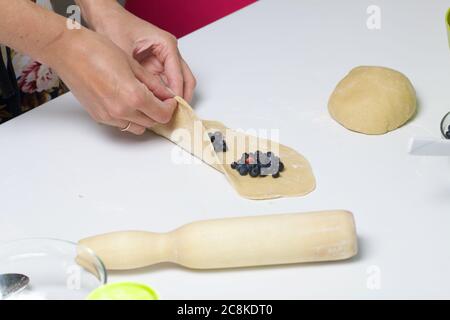 Eine Frau bereitet Knödel mit Heidelbeeren zu. Legt Beeren in gerollten Teig. In der Nähe auf dem Tisch sind ein Nudelholz und andere Kochwerkzeuge. Stockfoto