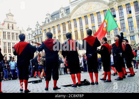 Eine Gruppe portugiesischer Universitätsstudenten, die am Grand Place in Brüssel Instrumente spielen und singen, winkt einer großen Flagge Portugals. Stockfoto