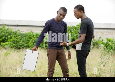 Zwei junge Studenten diskutieren draußen stehen und machen eine Handbewegung mit einem Computer in den Händen Stockfoto