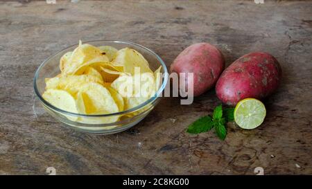 Kartoffelchips in einer Schüssel mit zwei rohen Kartoffeln und Zitrone Stockfoto