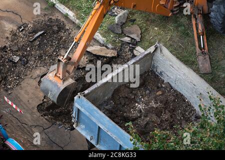 Der Bagger bricht den Asphalt. Durchbruch einer Wasserzuleitung. Das Wasser spülte den Asphalt weg. Stockfoto