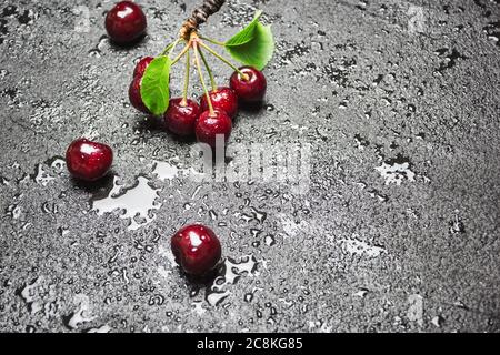 Frische reife Kirschen mit Blättern und Wassertropfen auf schwarzem Betongrund, Kopierraum. Stockfoto