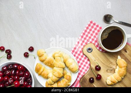 Frühstück mit hausgemachten Croissants, Kaffee und Süßkirschen auf hellem texturierten Hintergrund, Draufsicht mit Kopierraum. Stockfoto