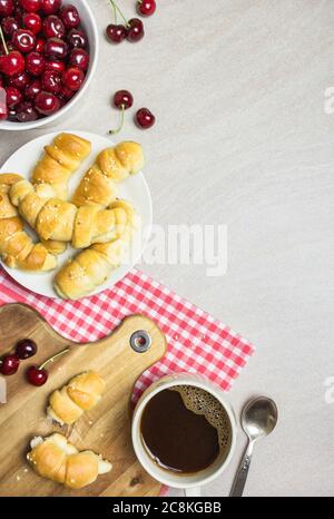 Frühstück mit hausgemachten Croissants, Kaffee und Süßkirschen auf hellem texturierten Hintergrund, Draufsicht mit Kopierraum. Stockfoto