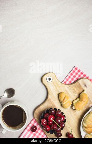 Frühstück mit hausgemachten Croissants, Kaffee und Süßkirschen auf hellem texturierten Hintergrund, Draufsicht mit Kopierraum. Stockfoto